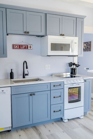 A kitchen with blue cabinets, a white microwave, a stove, and a sink.