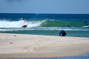 Una playa con olas, una persona haciendo surf y otra caminando por la orilla.