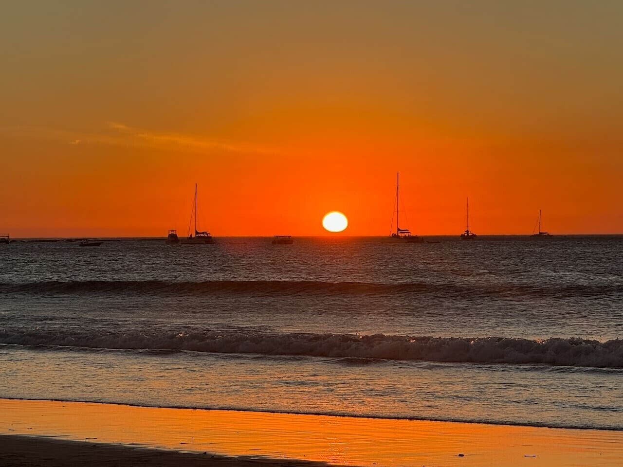 A sunset over the ocean with boats and a clear sky.