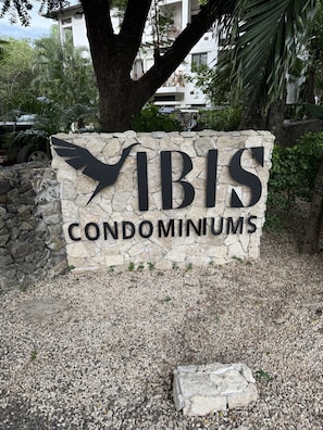 Schild für 'VIBIS CONDOMINIUMS' mit einer Steinsäule im Hintergrund und einer Palme.