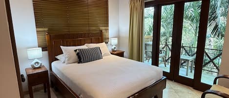 A bedroom with a large bed, a ceiling fan, a nightstand with a lamp, and a view of the outdoors through a glass door.