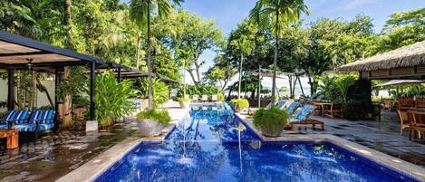Une piscine entourée d’une végétation tropicale, avec des chaises longues et des parasols.