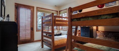 A room with bunk beds, a dresser, and a window with blinds.