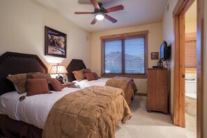 Ein Schlafzimmer mit zwei Betten, einem Deckenventilator, einem Fenster mit Jalousien, einem Holzschrank und einem Bild an der Wand.