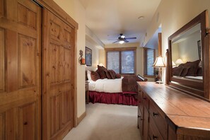 Une chambre avec une armoire en bois, un lit avec des rideaux rouges, un ventilateur de plafond et un grand miroir.