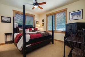 Une chambre à coucher avec un lit à baldaquin, deux fenêtres équipées de stores, un ventilateur de plafond, un bureau et une chaise.