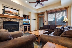 A living room with a fireplace, a television, and a stone wall. - AL4109 | Private Courtyard with Hot Tub | Pools | Close to Base | Air Chilling (Steamboat Springs)