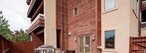 A multi-story building with a wooden exterior, balconies, and a small outdoor grill area. - AL4109 | Private Courtyard with Hot Tub | Pools | Close to Base | Air Chilling (Steamboat Springs)