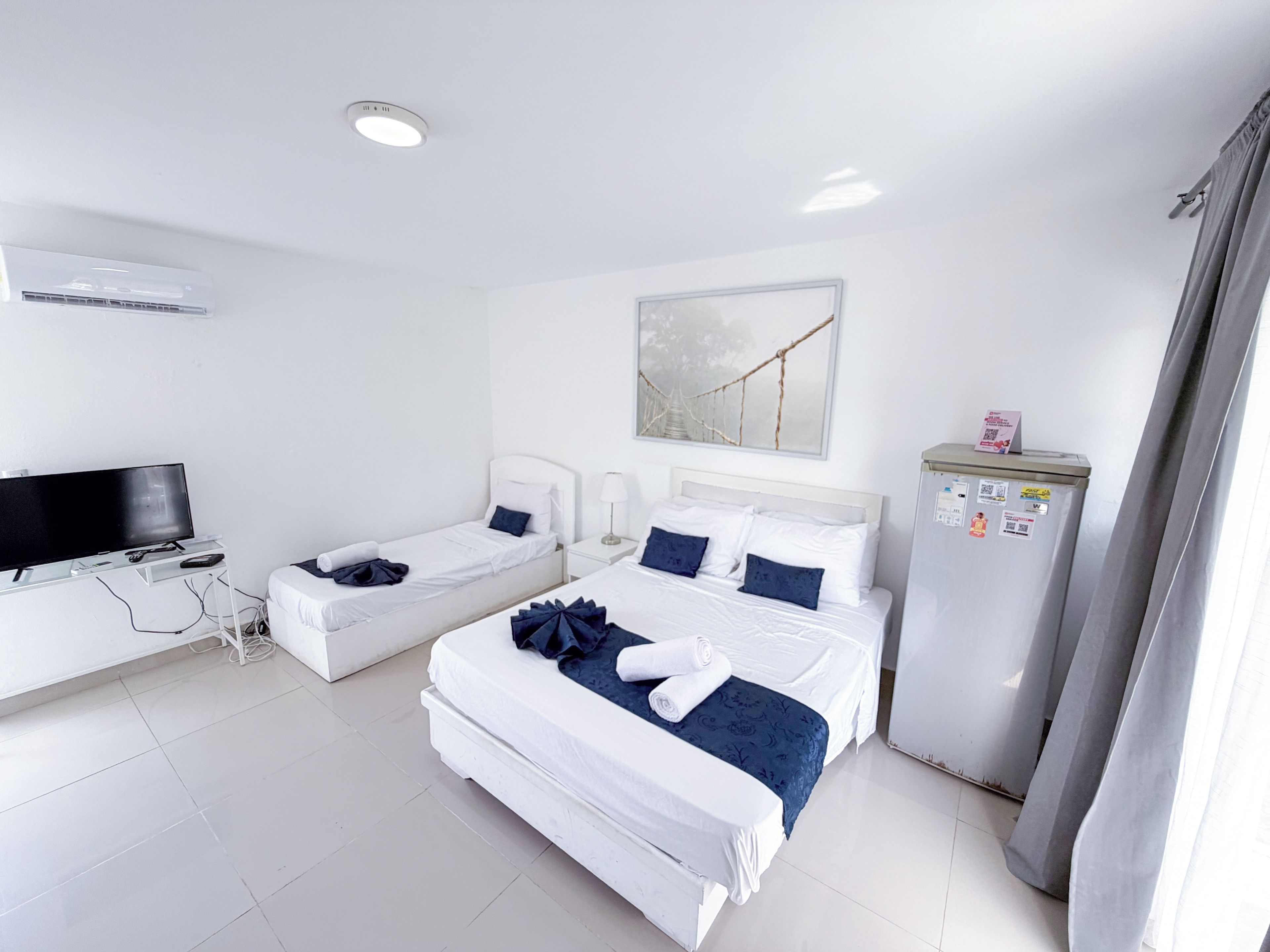 Habitación de hotel con dos camas, televisión, refrigerador y ventana con cortinas.