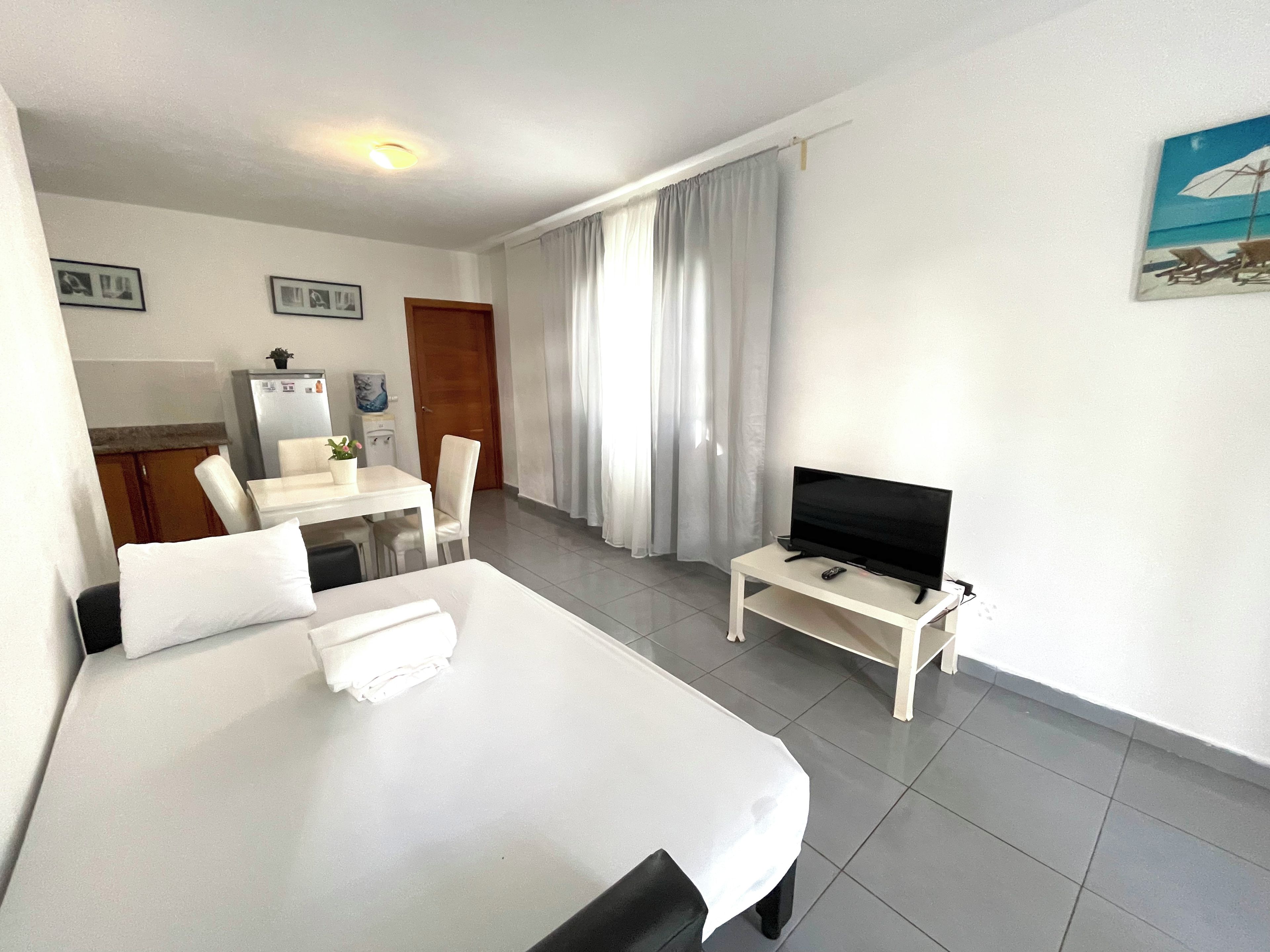 Habitación de hotel con cama, televisor sobre una mesita, una mesa de comedor con sillas y un área de cocina.