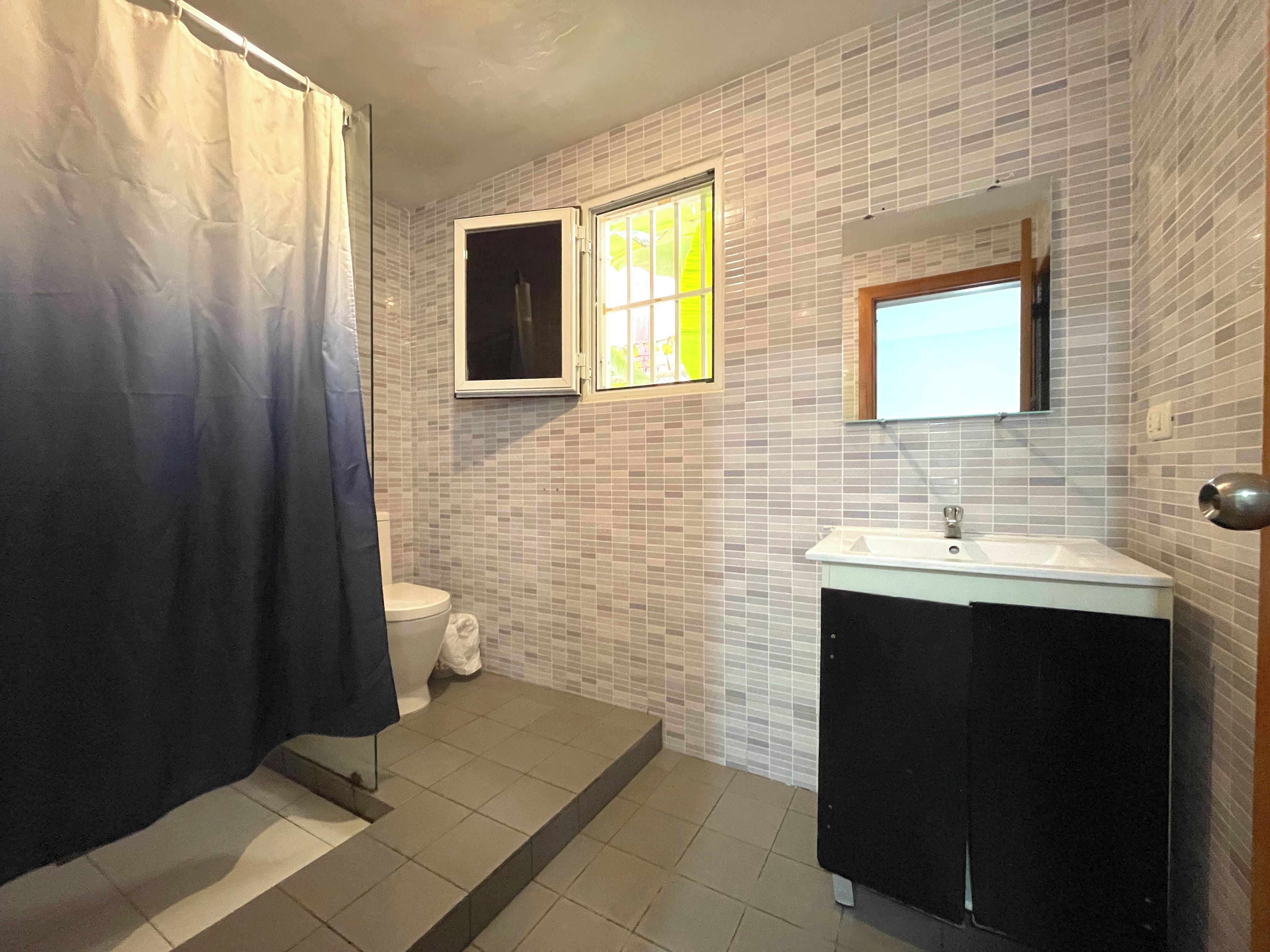 Ein Badezimmer mit Duschvorhang, Toilette, Waschbecken und einem Fenster.
