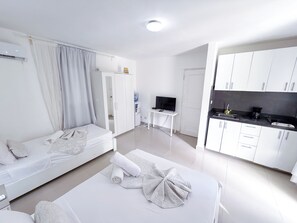 Ein modernes Hotelzimmer mit Bett, Fernseher, kleinem Tisch und Küchenzeile.