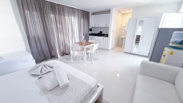 Una habitación de hotel moderna con cama, una pequeña mesa de comedor con sillas, kitchenette y baño con lavamanos e inodoro.