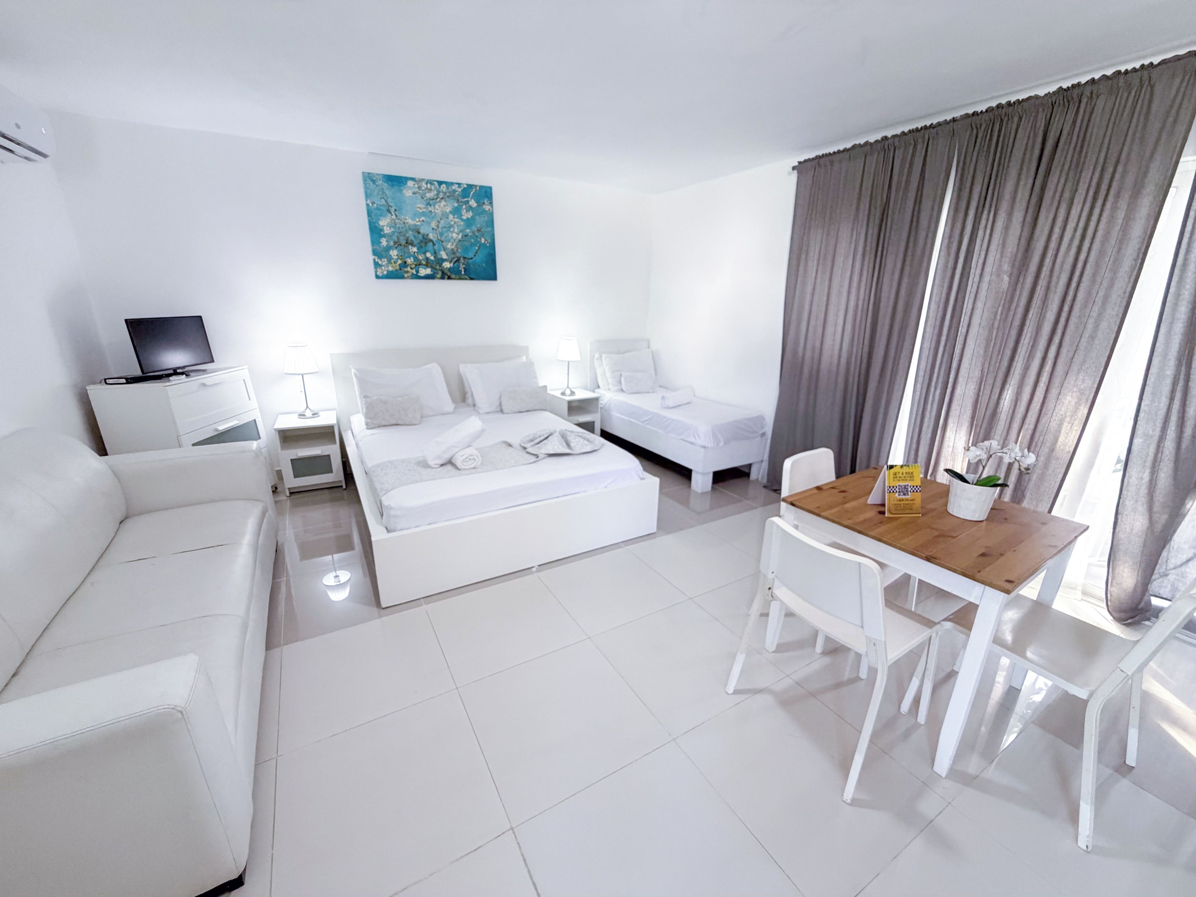 Habitación de hotel con cama, sofá, escritorio y sillas, televisión y un cuadro en la pared.