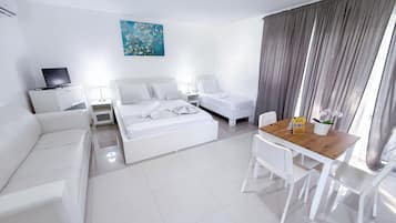 Habitación de hotel con cama, sofá, escritorio y sillas, televisión y un cuadro en la pared.