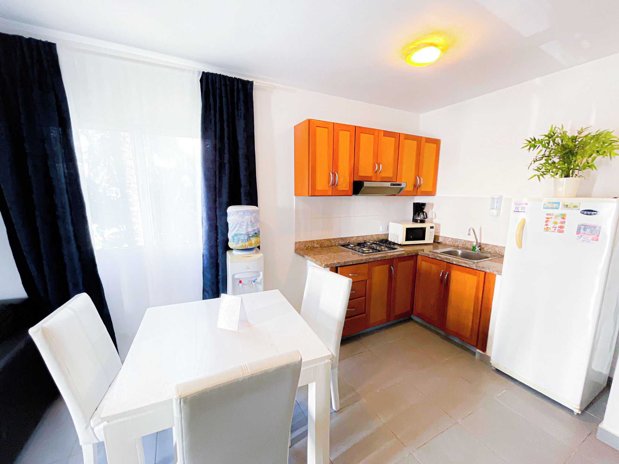 Una cocina compacta con armarios blancos, un refrigerador blanco y una mesa de comedor con sillas.
