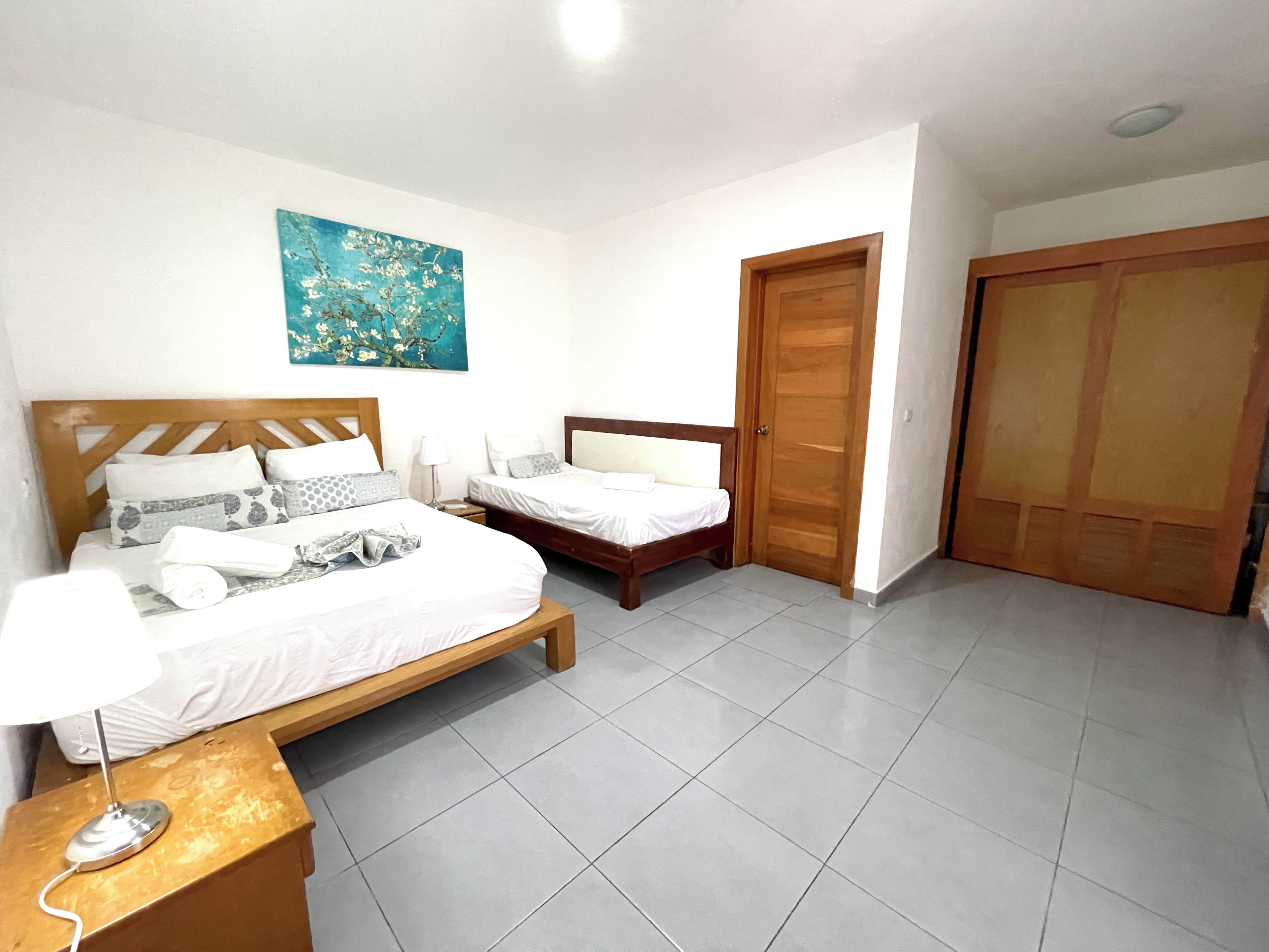 A bedroom with two beds, a wooden headboard, a bedside table with a lamp, and a painting on the wall.