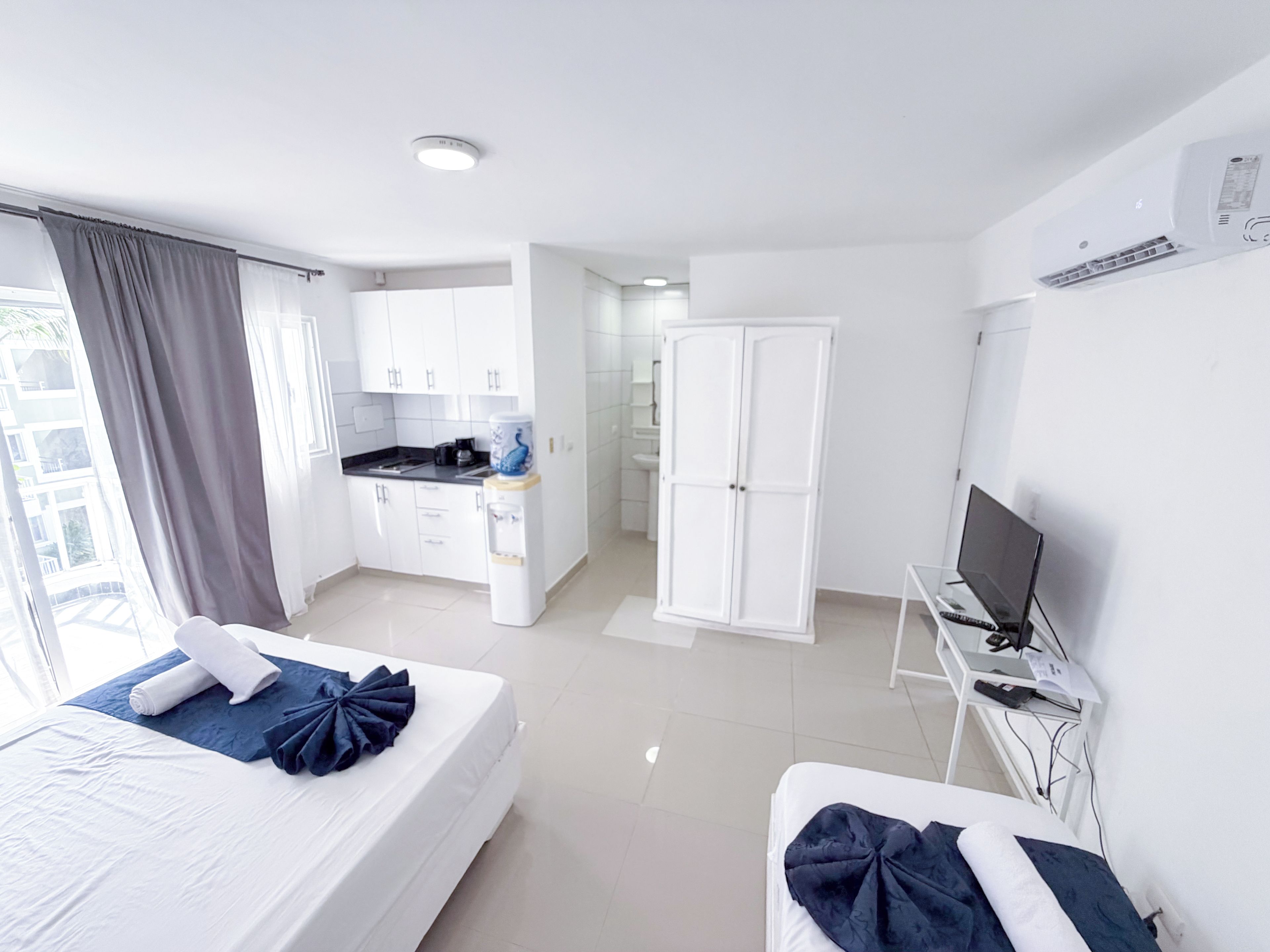 A hotel room with two beds, a kitchenette, a wardrobe, and a television.