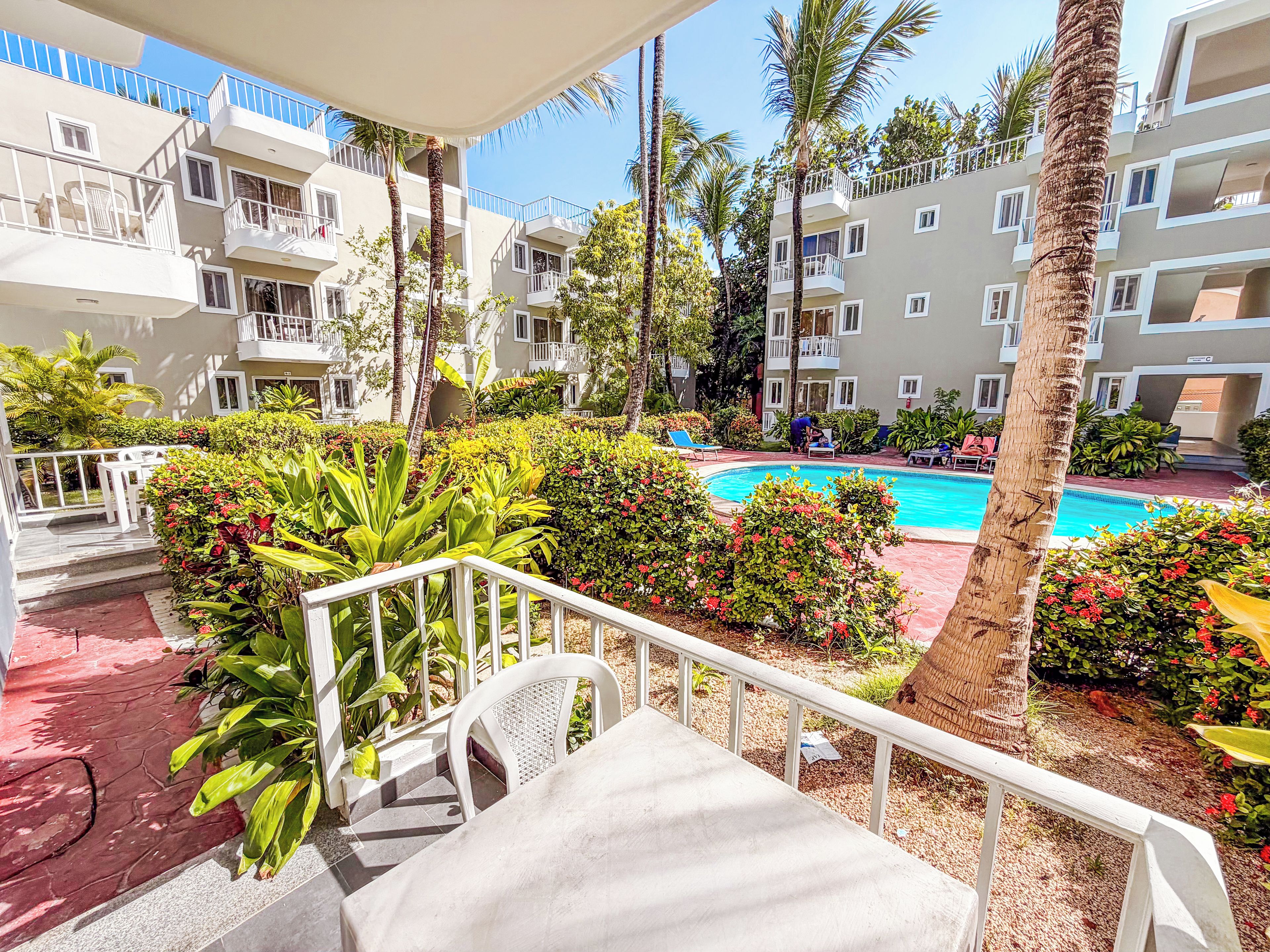 A hotel pool area with a clear view of the pool, surrounded by lush greenery and palm trees.