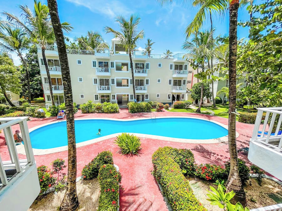 A hotel with a swimming pool surrounded by palm trees and a red-tiled walkway.
