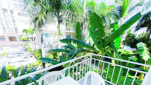 Un balcón con sillas y una mesa blancos, rodeado de exuberante follaje y vistas a una zona residencial.