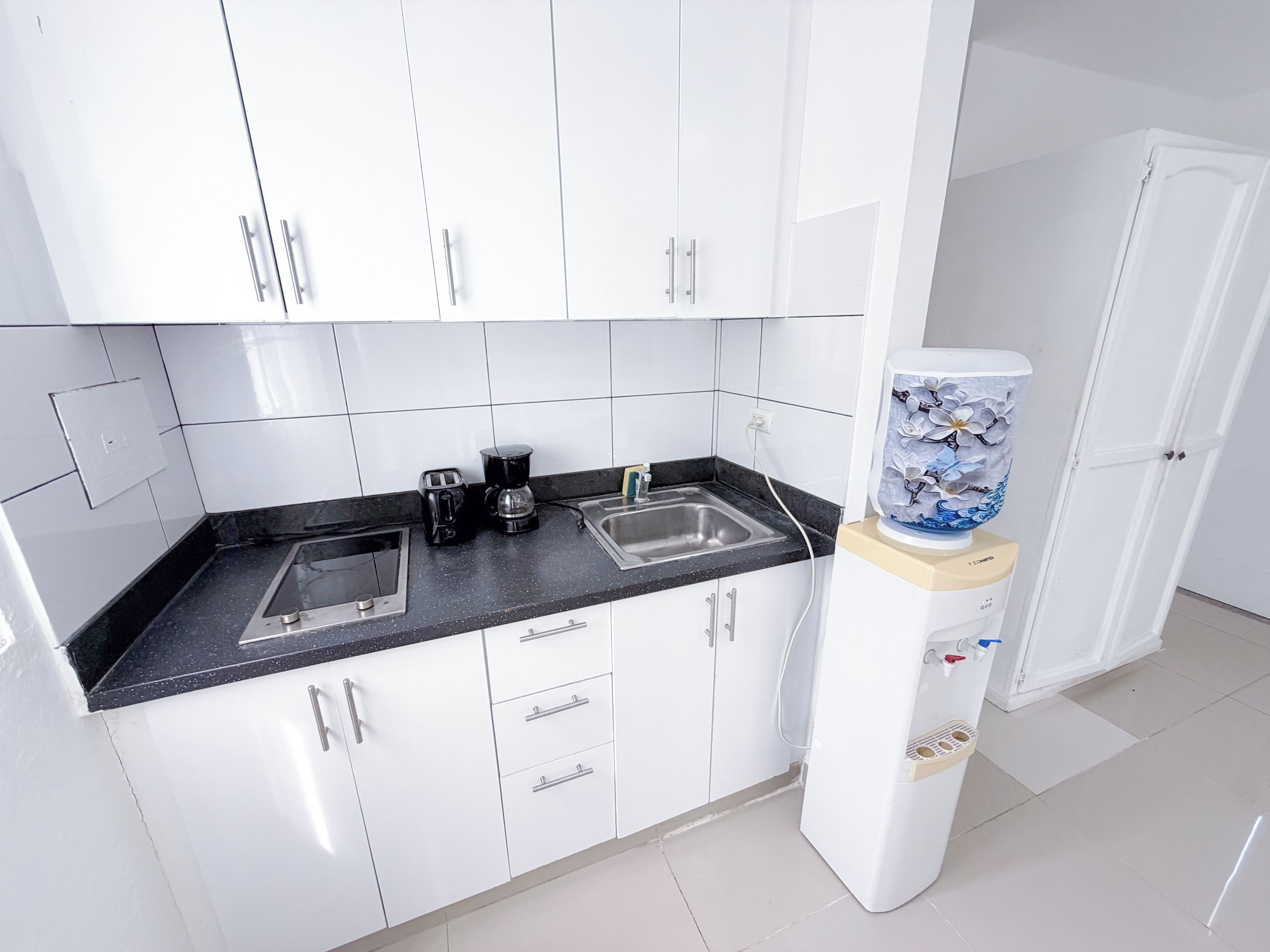 A modern kitchen with white cabinets, a black countertop, a coffee maker, a toaster, and a water dispenser.