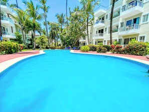 Une piscine entourée de palmiers et un immeuble à plusieurs étages doté de balcons.