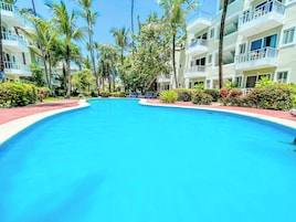 A swimming pool surrounded by palm trees and a multi-story building with balconies.