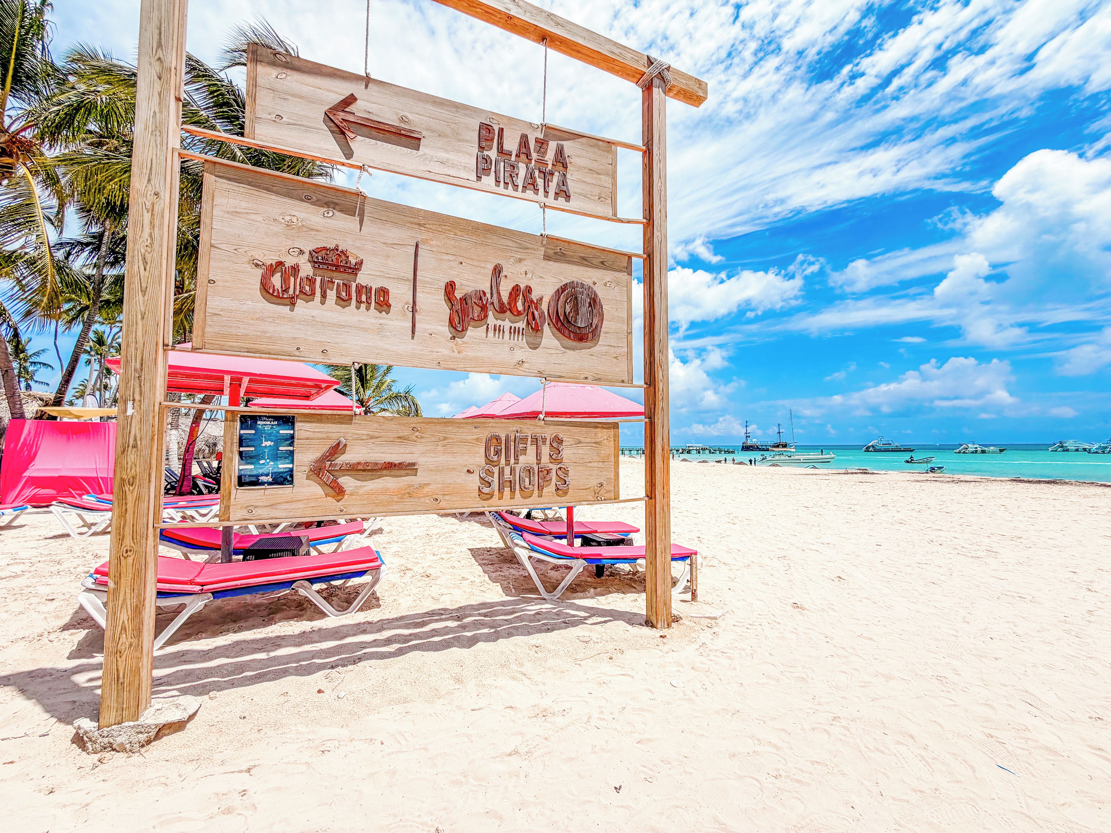 A wooden signpost with directional arrows and labels for a beach area, including a gift shop and a plaza.