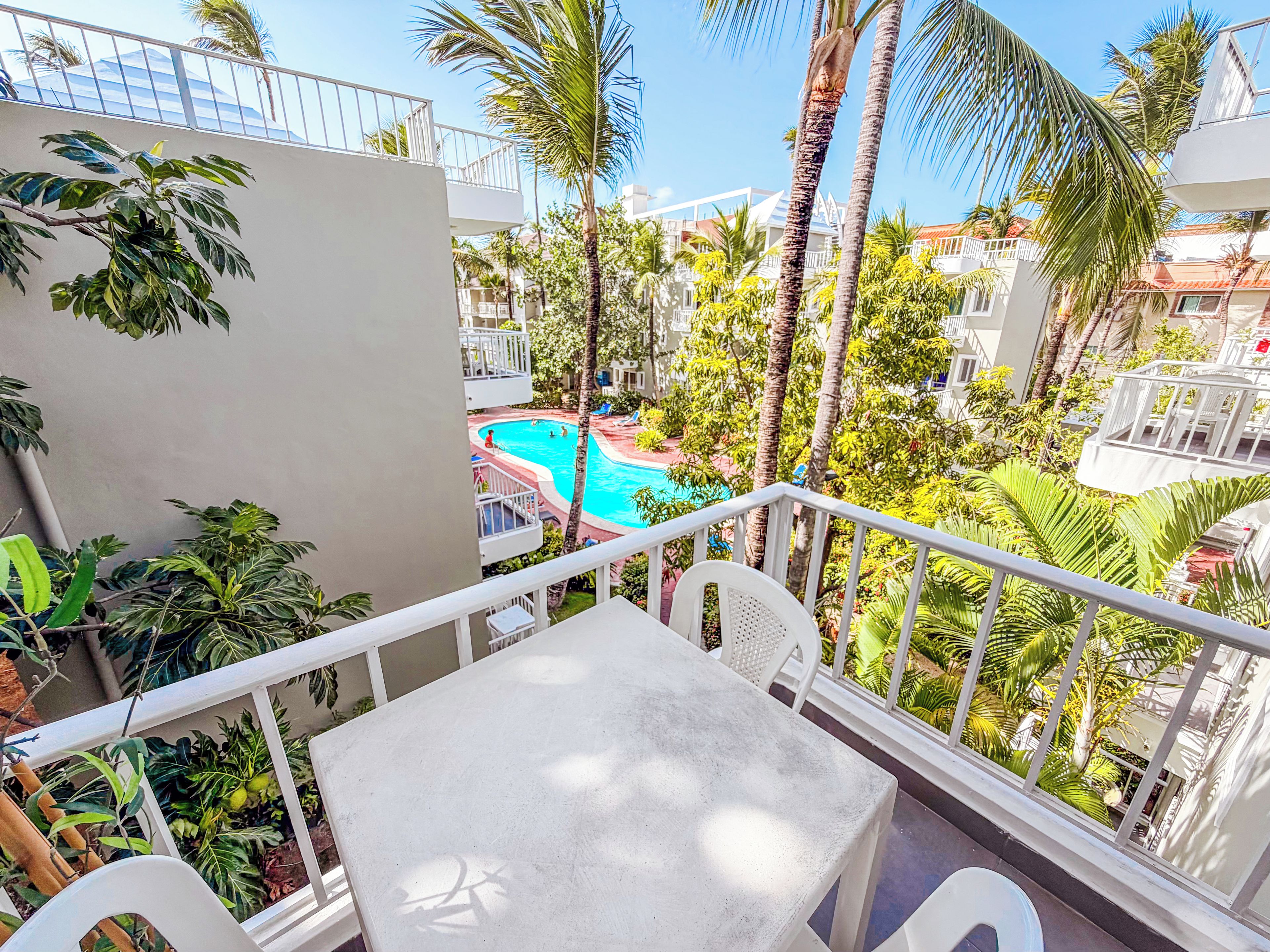 A balcony with a view of a swimming pool, surrounded by palm trees and other greenery.