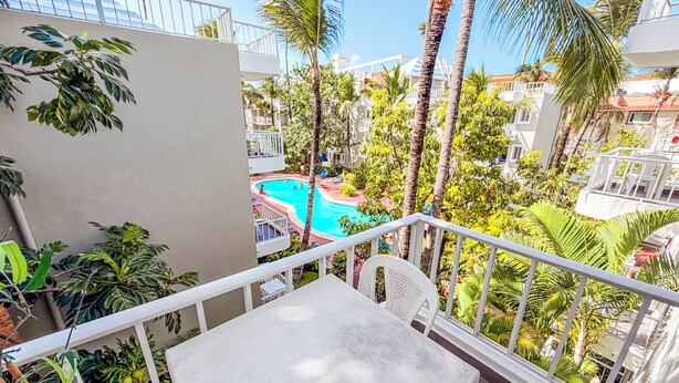 Un balcón con vista a una piscina, rodeado de palmeras y otra vegetación.