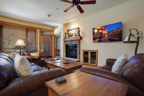 A living room with leather sofas, a wooden coffee table, a fireplace, and a television mounted on the wall. - AL4202 | Perfect Family Retreat | Mtn Views | Pools | Hot Tubs | Air Chilling (Steamboat Springs)