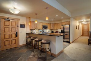Une cuisine moderne avec des meubles en bois, un réfrigérateur en acier inoxydable et un coin bar avec des tabourets.