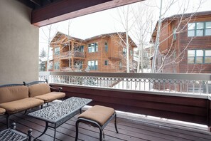 Eine Holzterrasse mit einer Couch und einem Tisch, mit Blick auf eine Reihe von Holzhäusern.