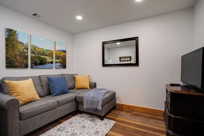 A living room with a grey sectional sofa, a flat-screen TV, a mirror, and two framed landscape paintings. - AL4203 | Beautiful and Professionally Decorated | 10 Hot Tubs | Air Chilling (Steamboat Springs)