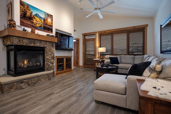 A living room with a stone fireplace, a sofa, and a television mounted on the wall. - AL4206 | Gorgeous Mountain Retreat | Close to Mountain | Pools | Air Chilling (Steamboat Springs)