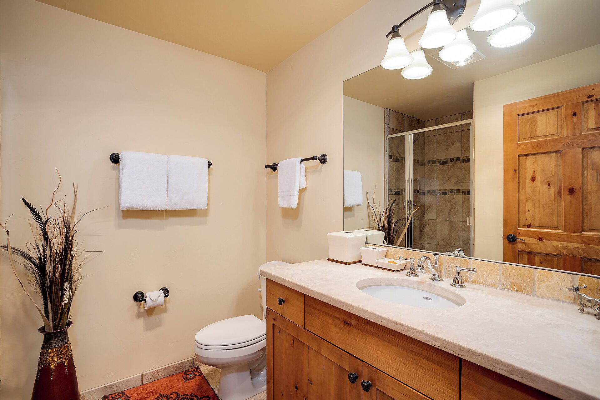 A bathroom with a toilet, sink, and mirror. There are towels hanging on hooks and a vase with dried plants.
