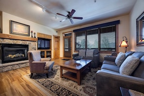 A living room with a fireplace, a ceiling fan, a sofa, a coffee table, and a television. - AL4207 | Sunset Views | Two Primary Bedrooms | Air Chilling | Close to Mtn (Steamboat Springs)