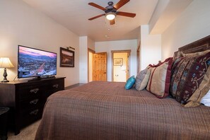 A bedroom with a large bed, a television on a dresser, a ceiling fan, and a door leading to another room. - AL4303 | Gorgeous Top Floor Condo | Close to Skiing | Air Chilling | Hot Tubs (Steamboat Springs)