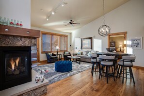 A modern living room with a fireplace, a dining area with bar stools, and a ceiling fan. - AL4305 | Top Floor Residence | Beautiful View | Air Chilling | 4 Pools (Steamboat Springs)