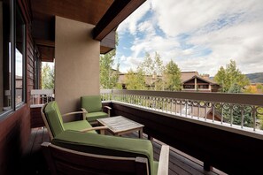 Een balkon met twee groene fauteuils en een klein houten tafeltje.