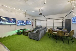 A room with a green carpet, a grey sofa, a wooden table, and two screens displaying 'Welcome to the Bear Cave.'