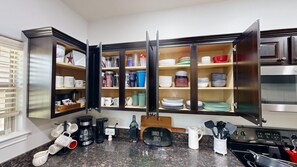 A kitchen with open cabinets displaying various dishes and utensils, a coffee maker, and a sign indicating dinner is served.