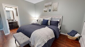 A bedroom with a bed, bedside table, lamp, and a small bench.