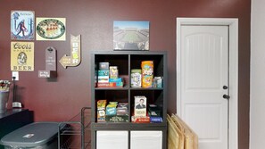 A room with a bookshelf containing board games, a door, and a wall with various posters and signs.