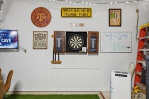 Um quarto com dardos, televisão e uma placa com a mensagem 'Bem-vindos à Toca do Urso'.