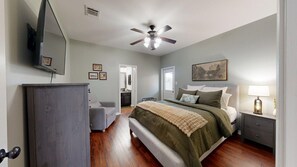 Quarto com cama, mesa de cabeceira, ventoinha no teto e porta que dá para o banheiro.