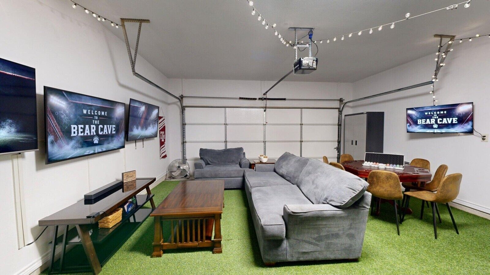 Een kamer met een grijze bank, een houten salontafel, een kleine televisie en een tafel met stoelen.