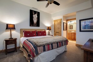 A bedroom with a large bed, two bedside lamps, a ceiling fan, a wooden door, and a bathroom visible through an open door. - BL6102 | Unforgettable Mtn Getaway | 4 Pools | Walk to Mountain | Air Chilling (Steamboat Springs)