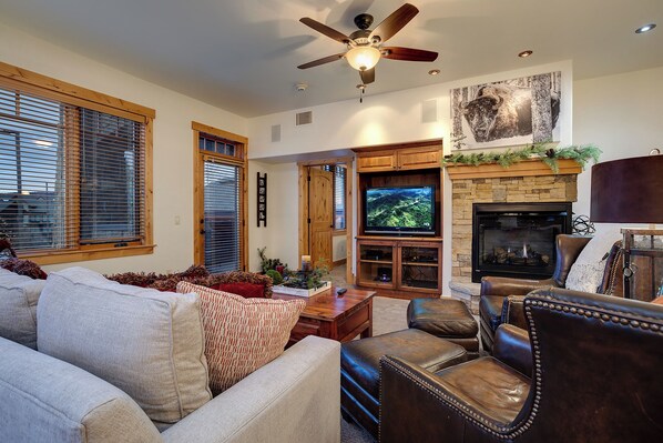 A living room with a fireplace, television, leather chairs, and a ceiling fan. - BL6102 | Unforgettable Mtn Getaway | 4 Pools | Walk to Mountain | Air Chilling (Steamboat Springs)